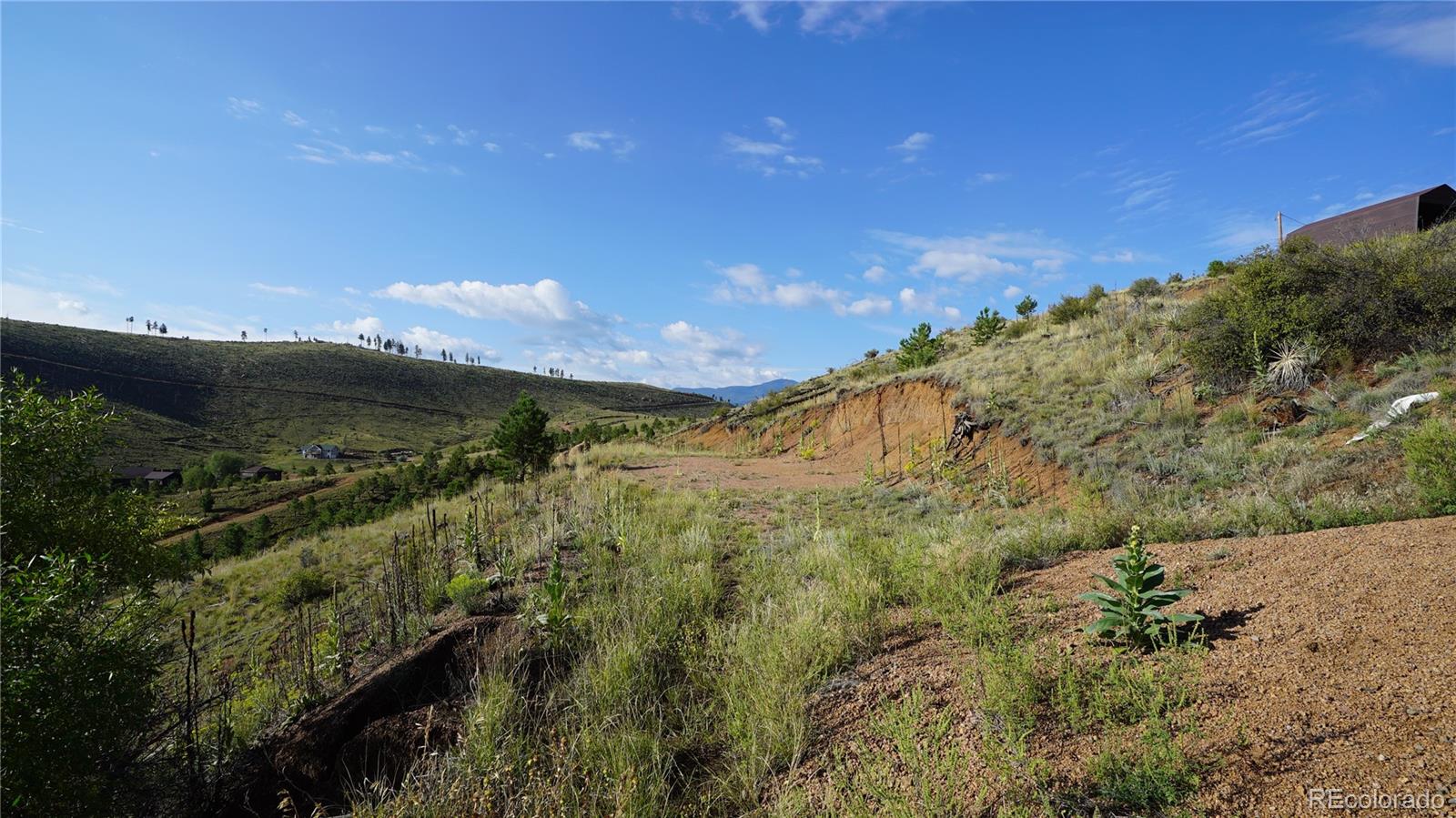 Vacant hillside land with a gravel track, valley homes, and distant mountain ridges.