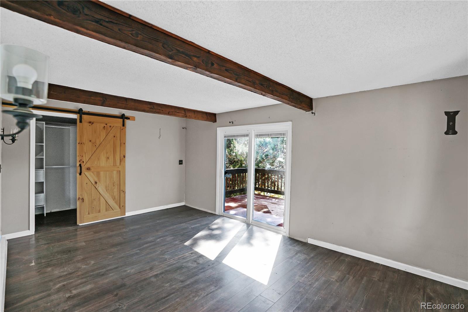 Empty room with exposed wood beams, a sliding barn door, and glass doors to a deck.
