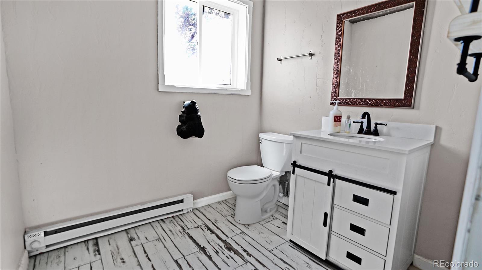 Bathroom with a white vanity, black hardware, and distressed white plank flooring.
