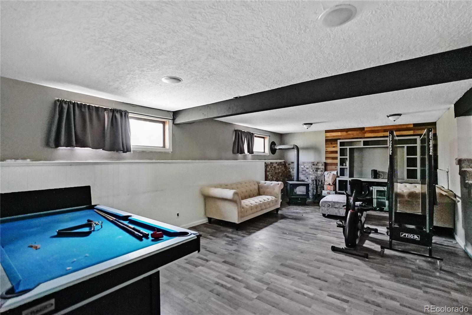 Basement recreation room with a blue pool table, cream sofa, wood stove, and exercise equipment.
