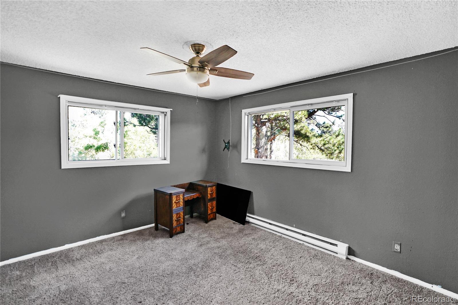 Gray-carpeted room with two windows, a ceiling fan, and a small wooden desk.