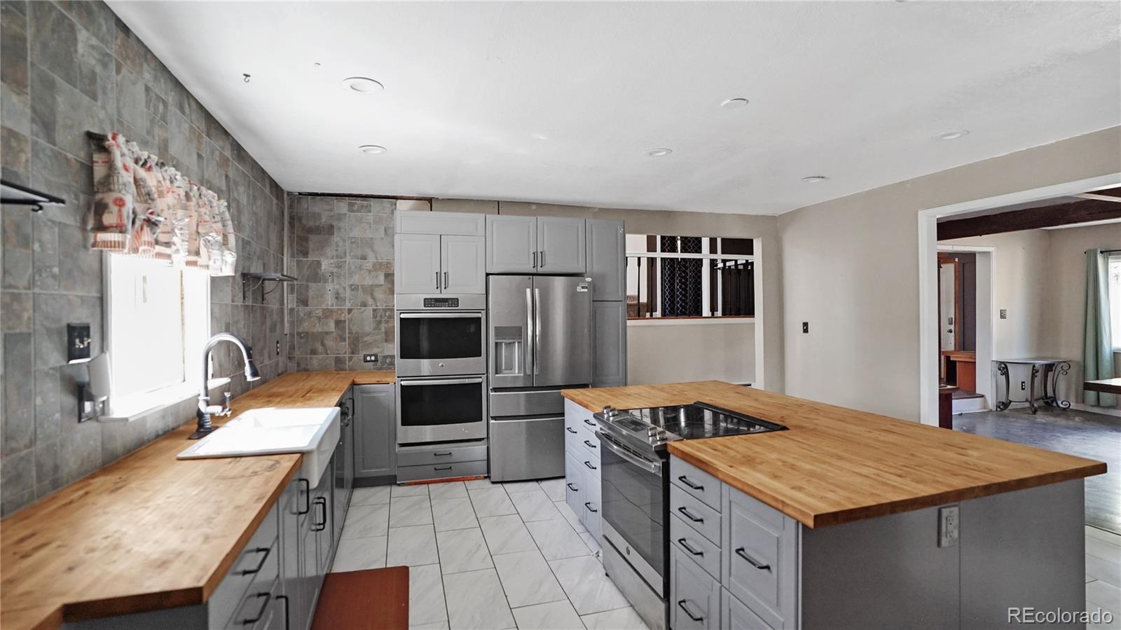 Kitchen with gray cabinetry, stainless appliances, butcher-block counters, and a large central island.