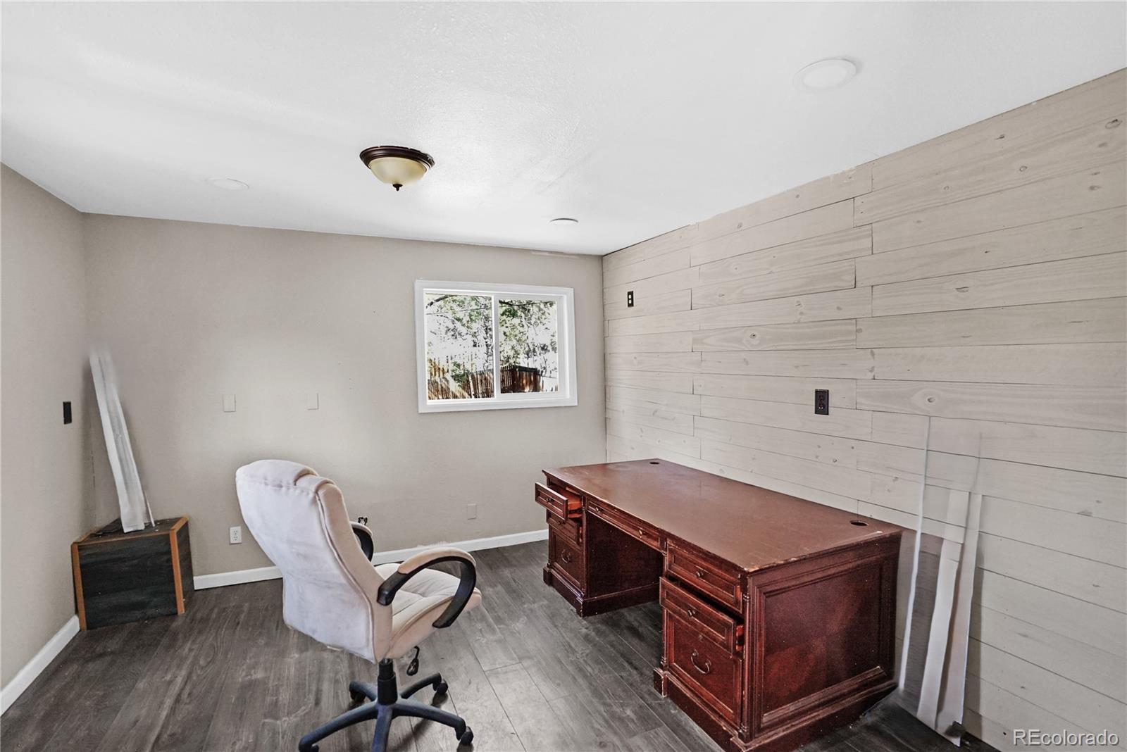 Home office with a whitewashed wood accent wall, dark desk, and gray plank flooring.