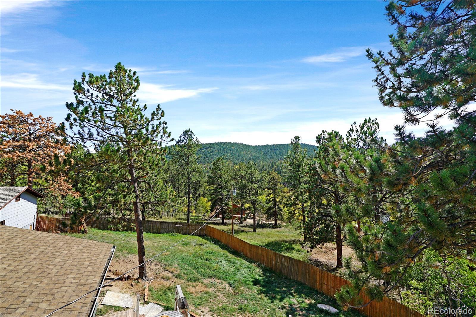 Fenced backyard with pine trees and a forested mountain view.