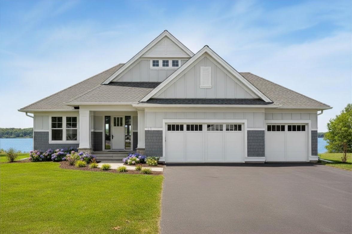White and gray gabled house with a three-car garage and lake visible behind it.