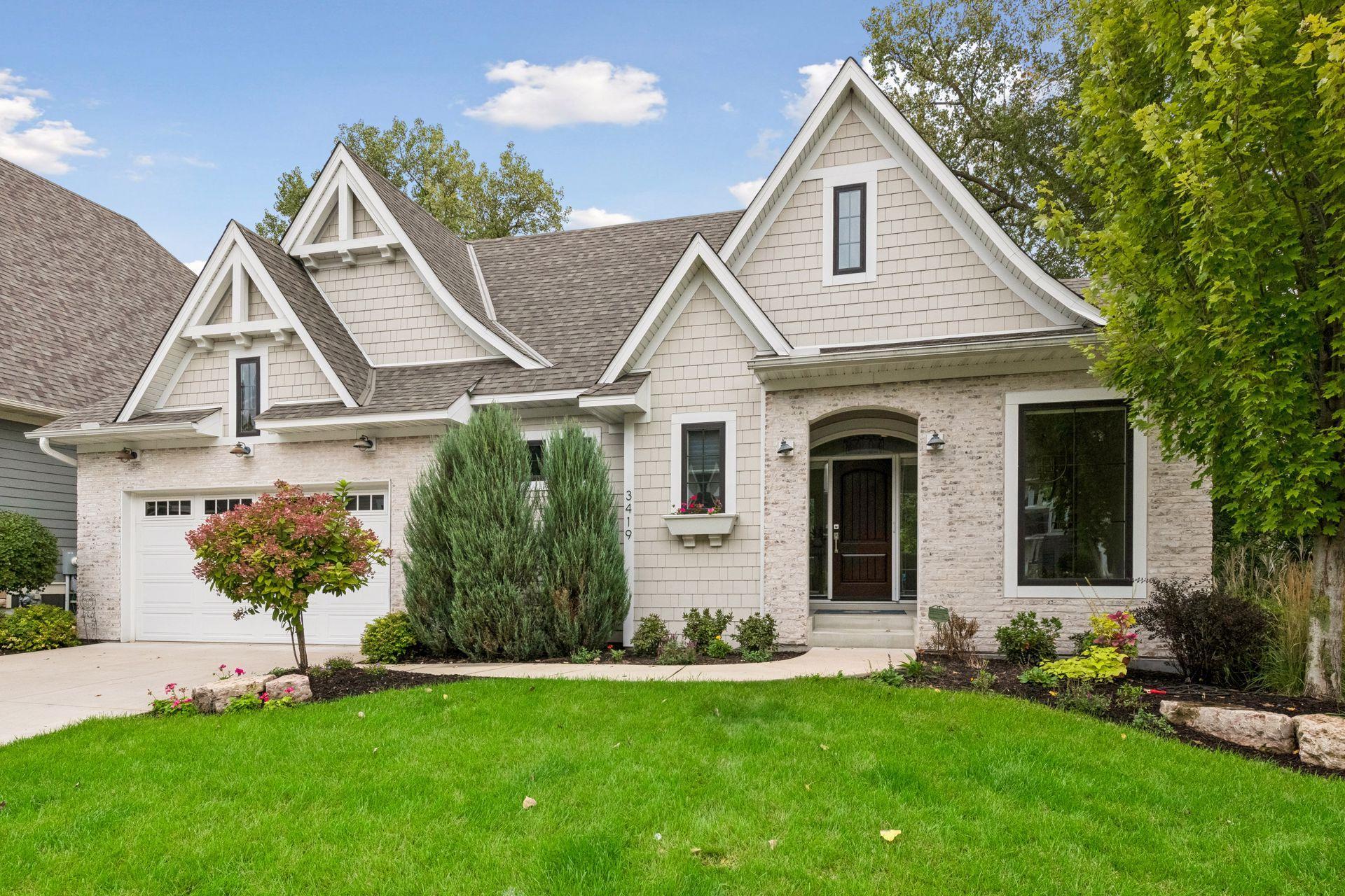 Light-colored shingle-and-stone home with multiple gables, an arched entry, and landscaped lawn.
