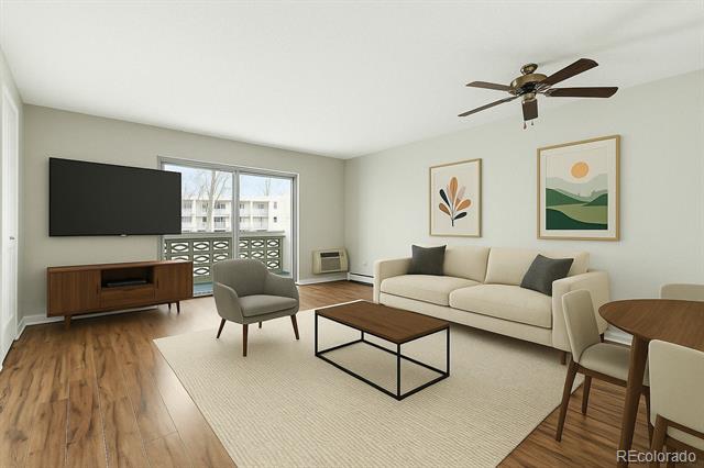 Staged living room with a cream sofa, gray chair, hardwood floors, and a sliding glass door to a balcony.