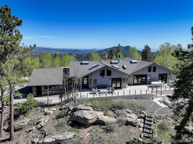 Modern gray home with roof skylights and a broad patio, backed by wooded mountain views.