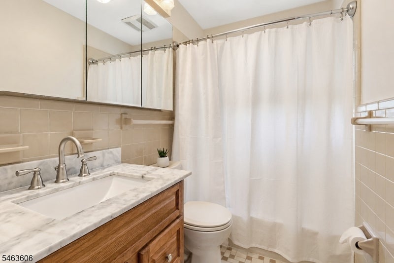 Bathroom with a marble-look vanity, mirrored cabinet, beige tile, and white shower curtain.