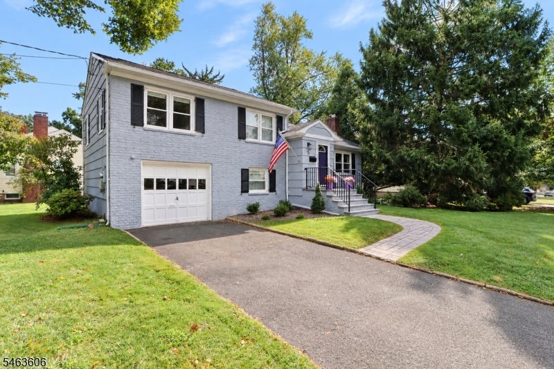 Two-story gray-brick house with attached garage, American flag, and curved front walkway.