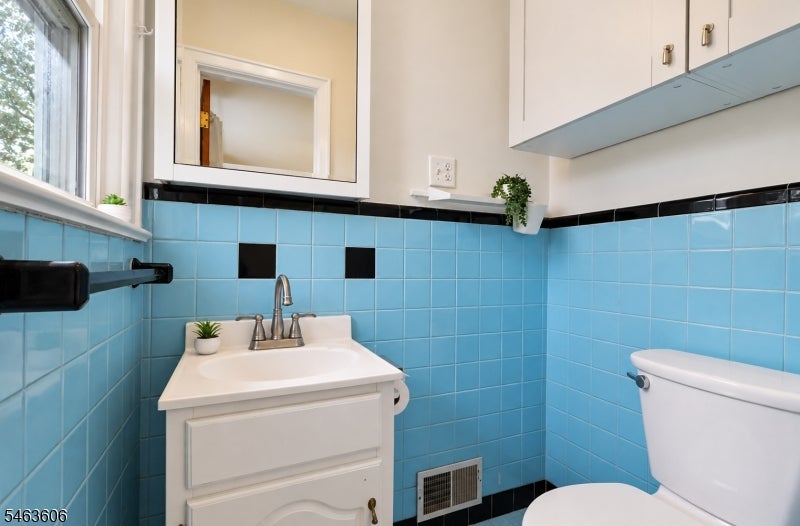 Bathroom with blue tile walls, white vanity, mirrored cabinet, and toilet.