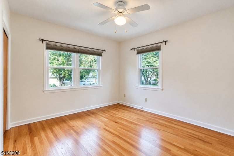 Vacant bedroom with polished hardwood floors, two windows, and a ceiling fan.