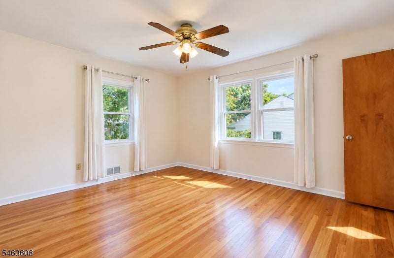 Unfurnished bedroom with polished hardwood floors, curtained windows, and a ceiling fan.