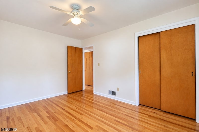 Empty bedroom with hardwood floors, a ceiling fan, and wooden closet doors.