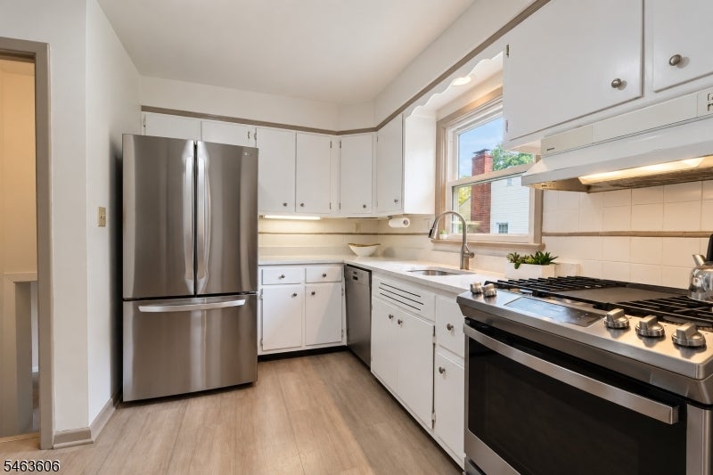 Kitchen with white cabinets, stainless steel appliances, and a black range beneath a stainless hood.