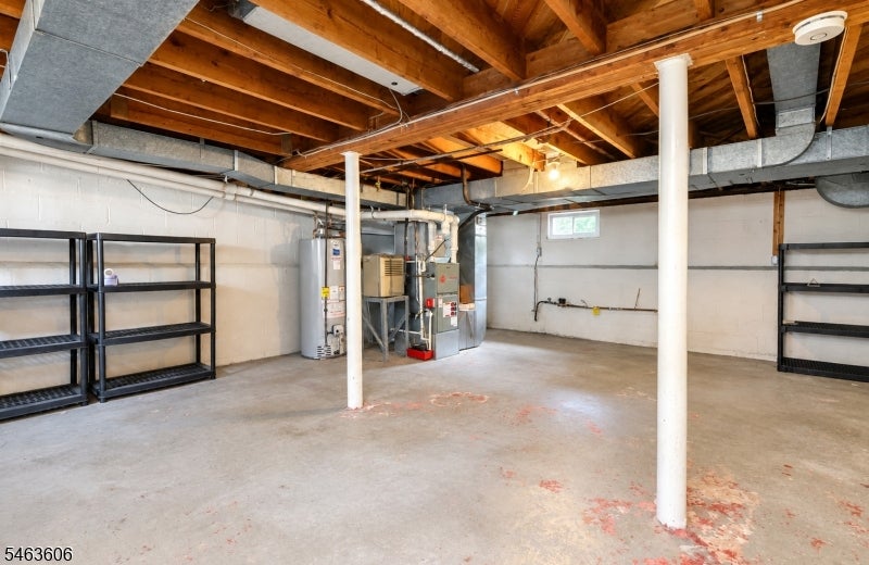 Unfinished basement with exposed ceiling joists, concrete floor, utility equipment, and metal shelving.