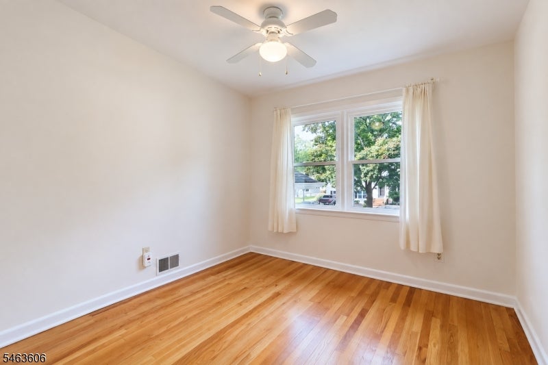 Empty bedroom with hardwood floors, curtained window, and ceiling fan with light.
