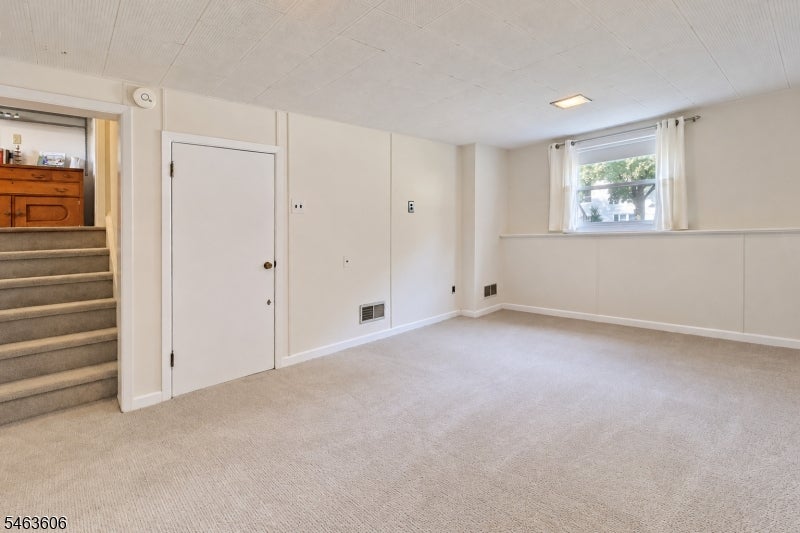 Empty carpeted room with a high window and stairs leading to an upper landing.