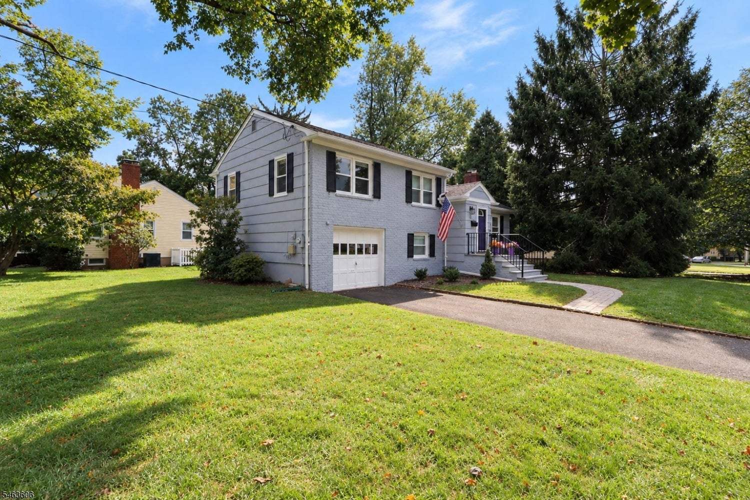 Light gray two-story house with an attached garage, curved front walkway, and American flag.