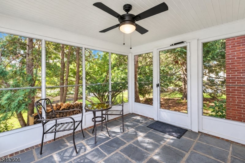 Enclosed sunroom with large windows, stone-tile floor, black metal seating, and a ceiling fan.