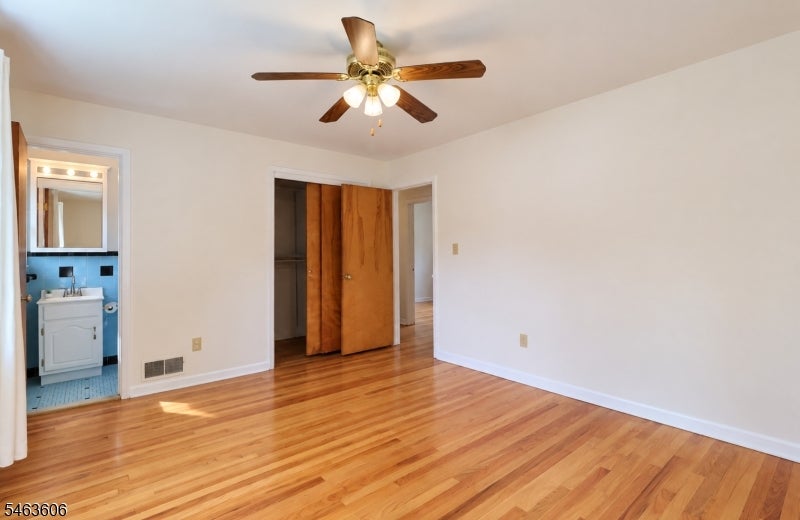Empty bedroom with hardwood floors, ceiling fan, and open closet beside an adjoining bathroom.