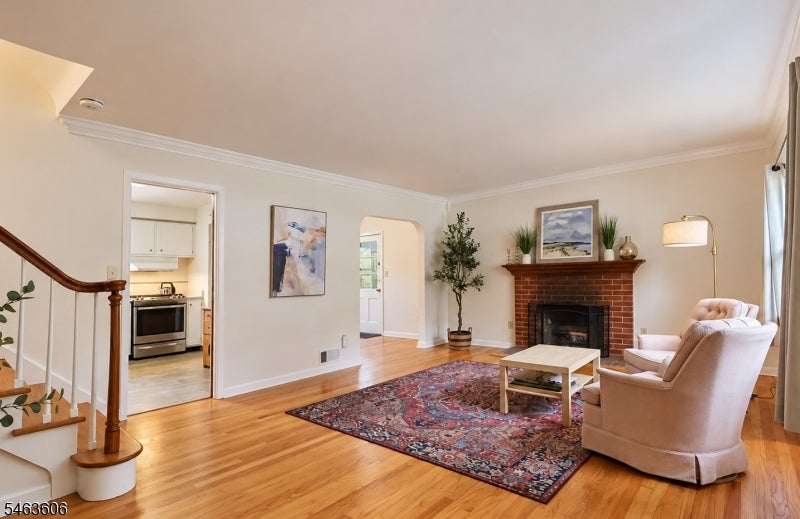 Living room with a brick fireplace, patterned rug, hardwood floors, and adjacent kitchen.