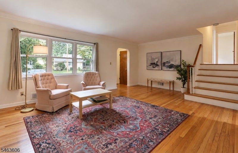 Living room with two armchairs, a patterned rug, large windows, and a staircase.