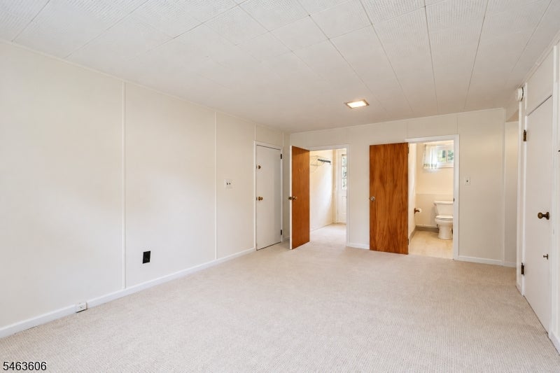 Empty carpeted bedroom with white walls and open doors to a bathroom and adjoining room.