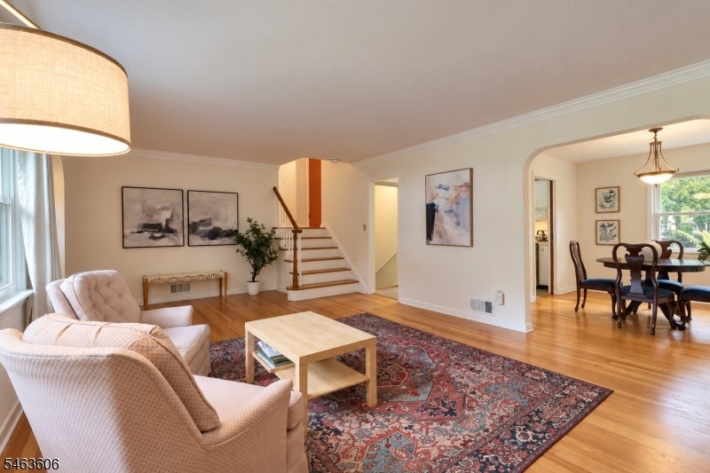Living room with a central staircase, patterned rug, pale seating, and an adjoining dining area.