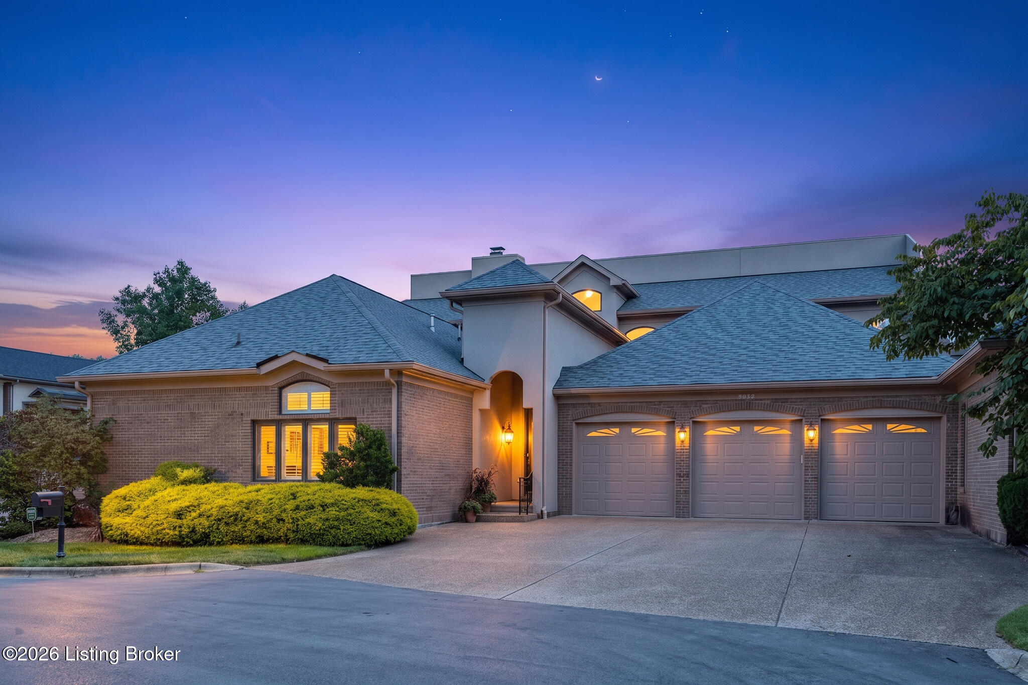 Brick house with a three-car garage and warmly lit entry at dusk.