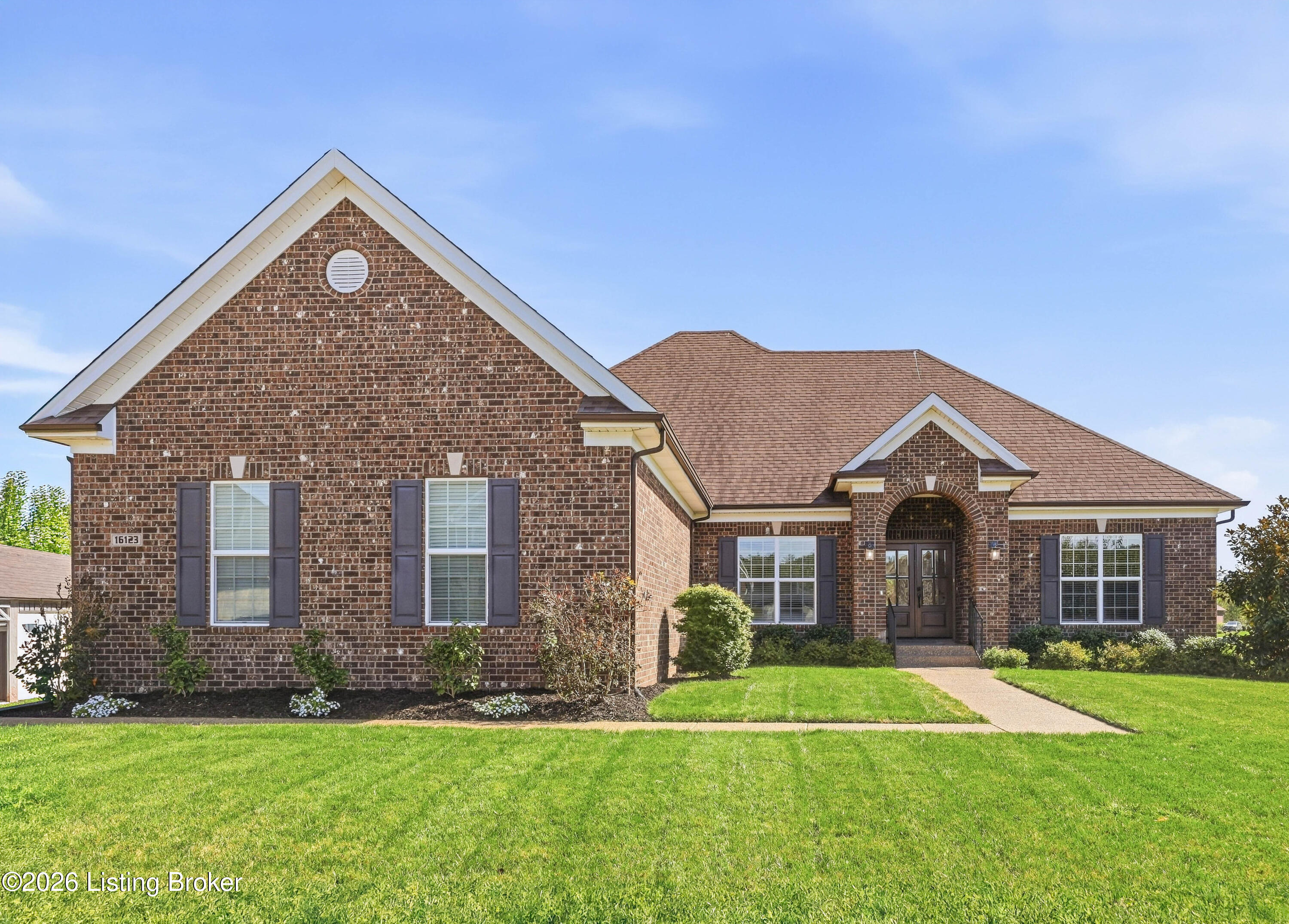 Red brick house with an arched entry, dark shutters, and a broad green front lawn.