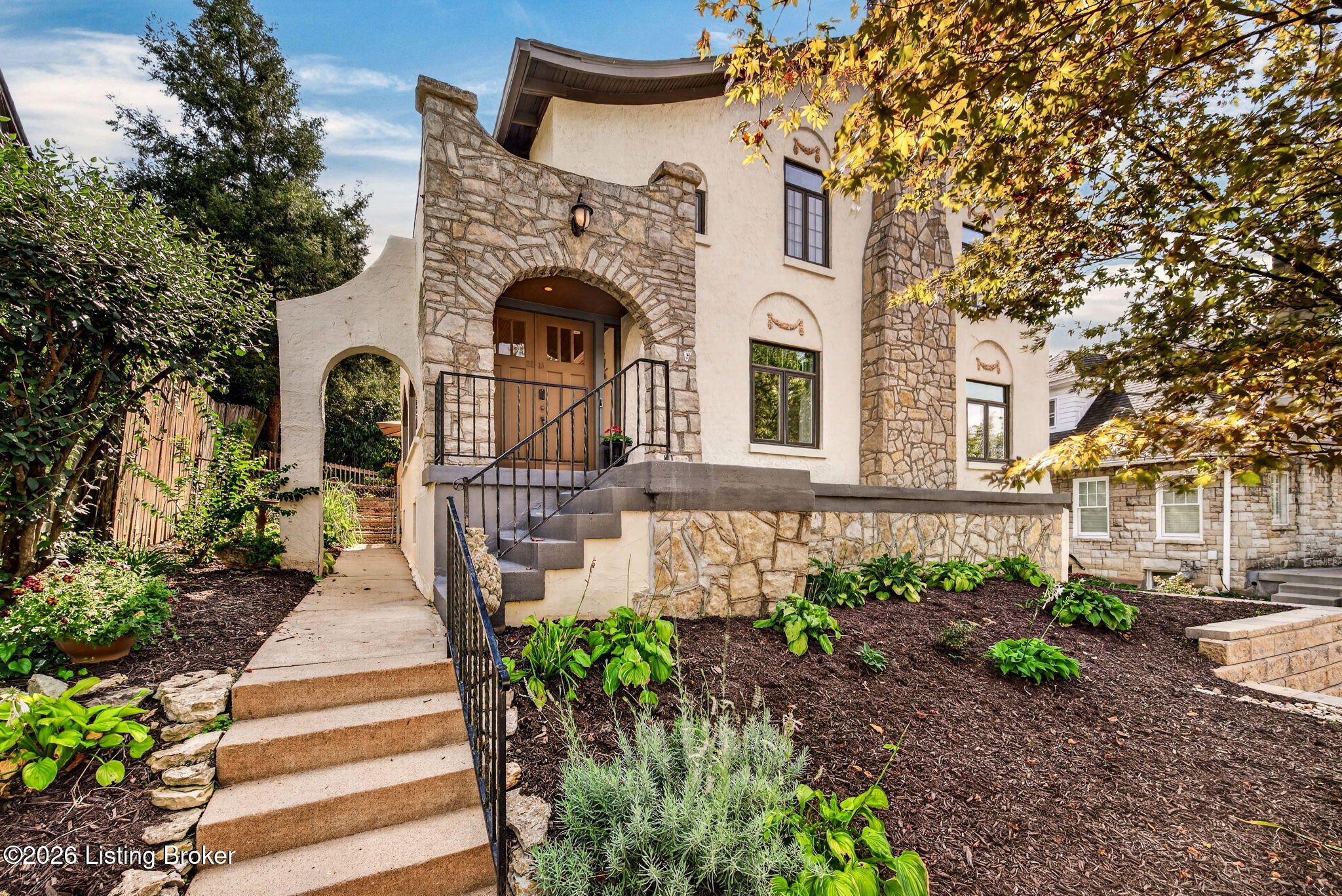 Two-story stucco and stone home with an arched entry, broad front steps, and landscaped garden.