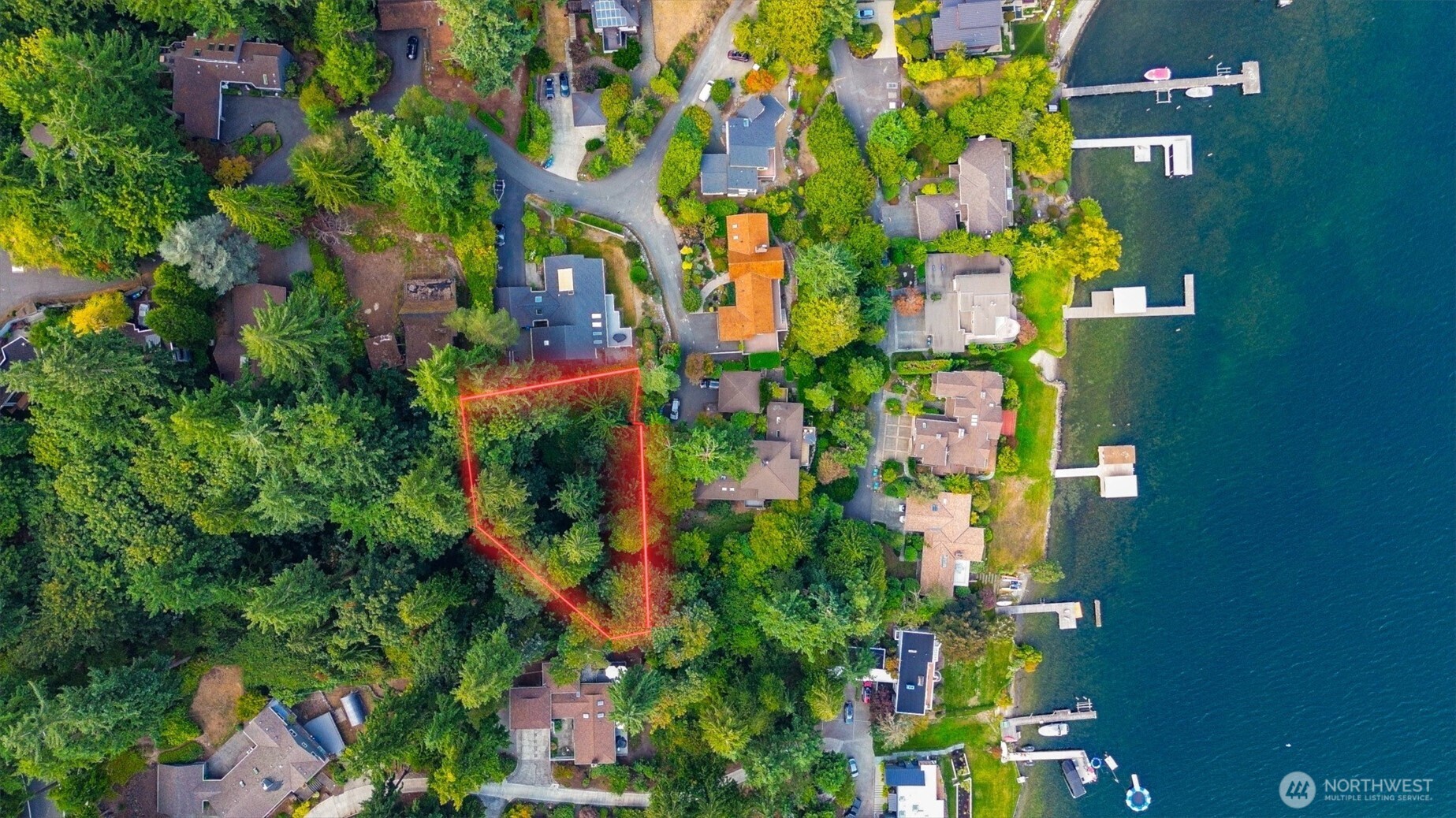 Aerial view of a wooded parcel outlined in red near shoreline homes and docks.