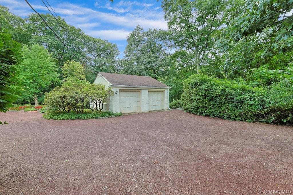 Detached two-car garage beside a broad gravel driveway, surrounded by mature trees and shrubs.