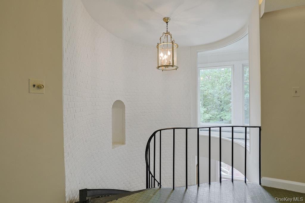 Stair landing with a curved black railing, white brick wall, brass pendant, and tall window.