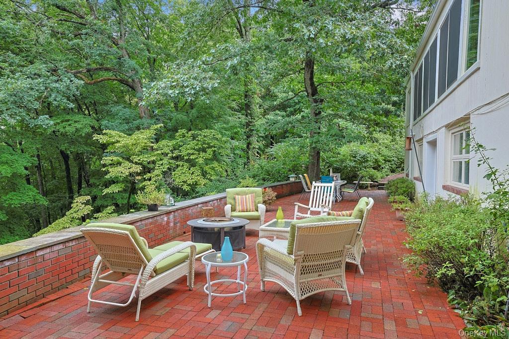Furnished brick patio beside the house, with wicker seating and a wooded backdrop.