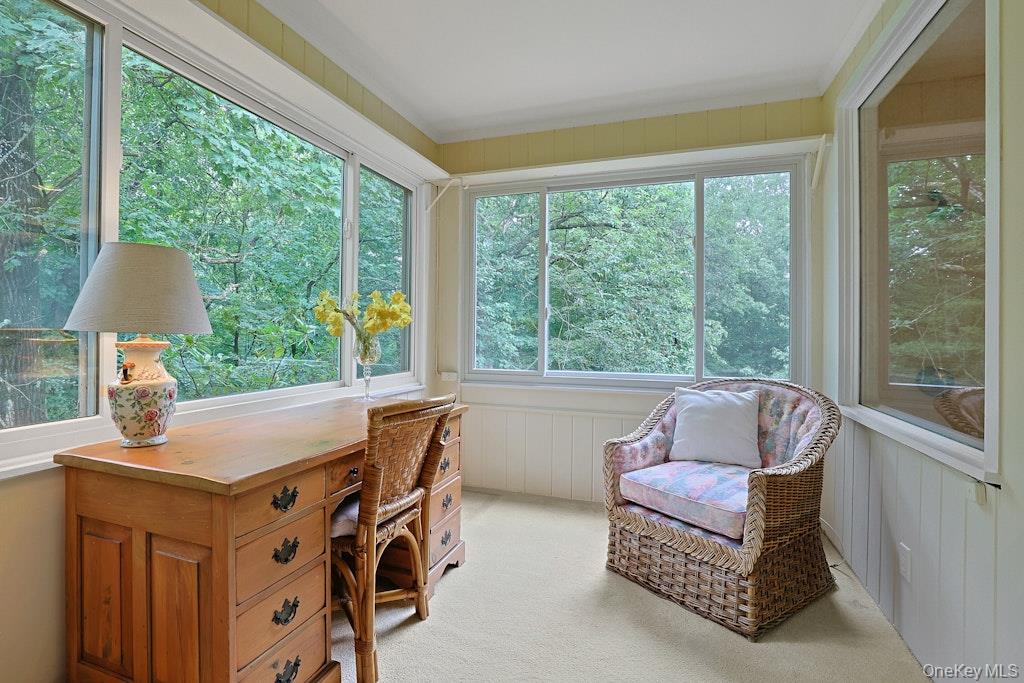 Sunroom with broad leafy views, a wooden desk, and a floral wicker armchair.