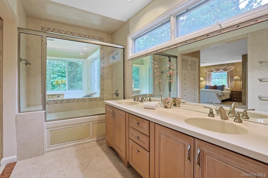 Bathroom with a long double vanity, glass-enclosed tub, and broad windows.