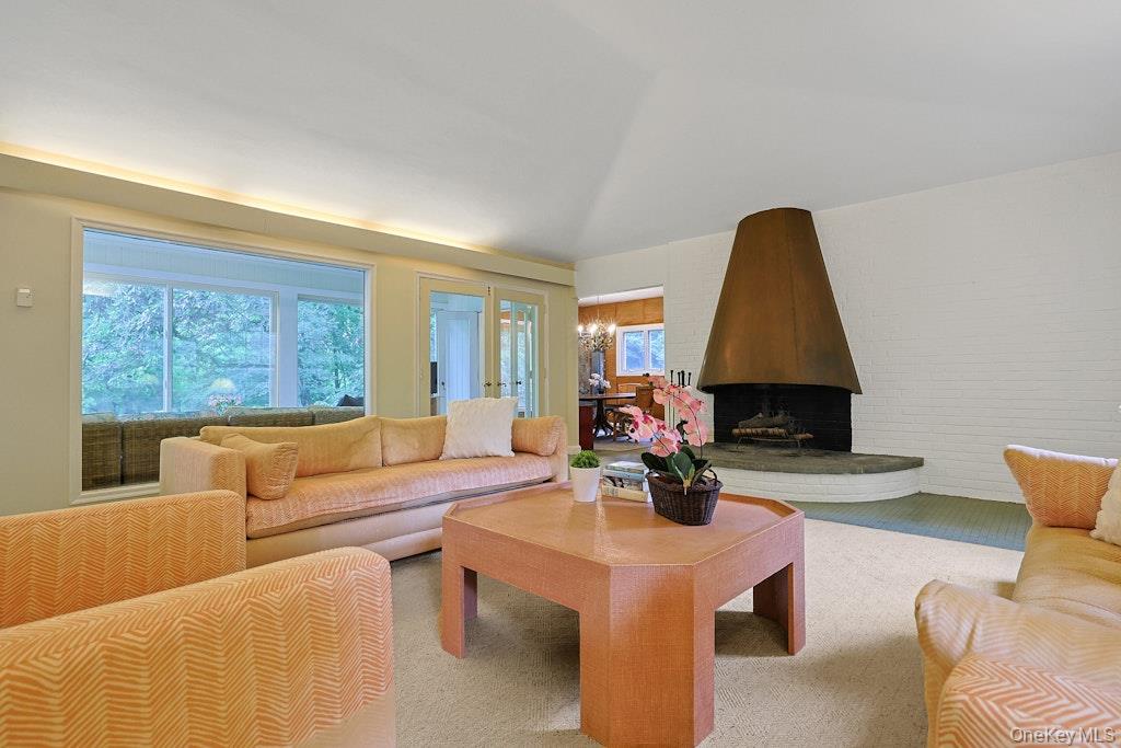 Living room with a large tapered fireplace, broad tree-facing windows, and peach-toned seating.