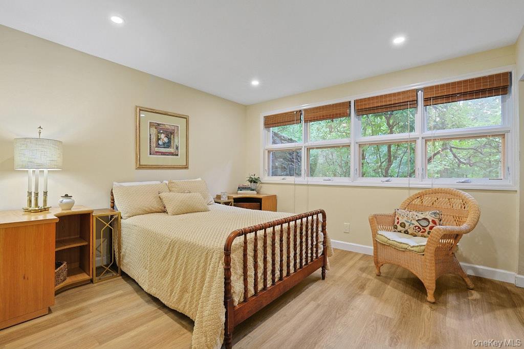 Furnished bedroom with a wooden spindle bed, cream bedding, wicker chair, and wide windows overlooking trees.