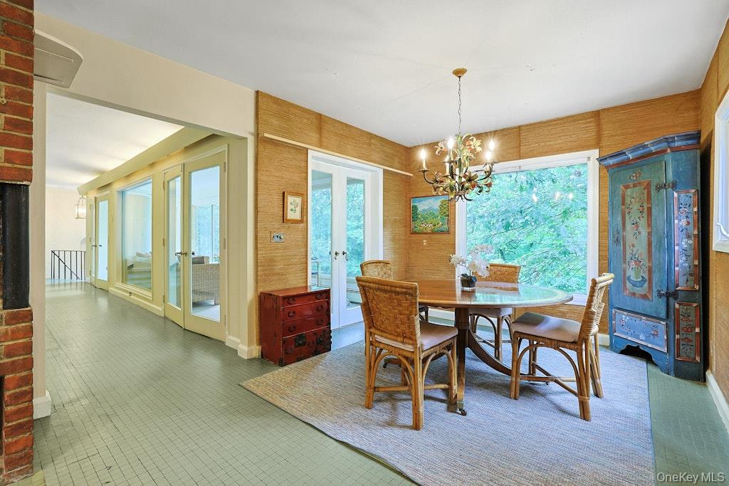 Dining room with a round table, wicker chairs, chandelier, blue cabinet, and large windows overlooking trees.