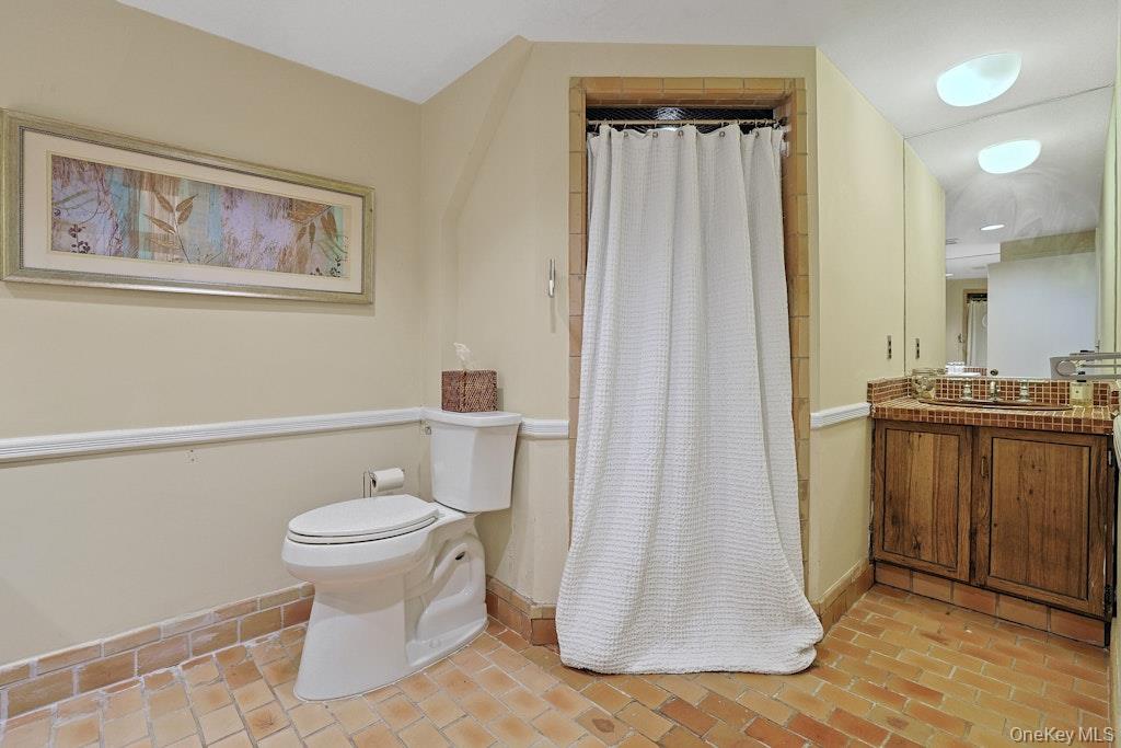 Bathroom with a white shower curtain, wood vanity, and warm-toned tile floor.