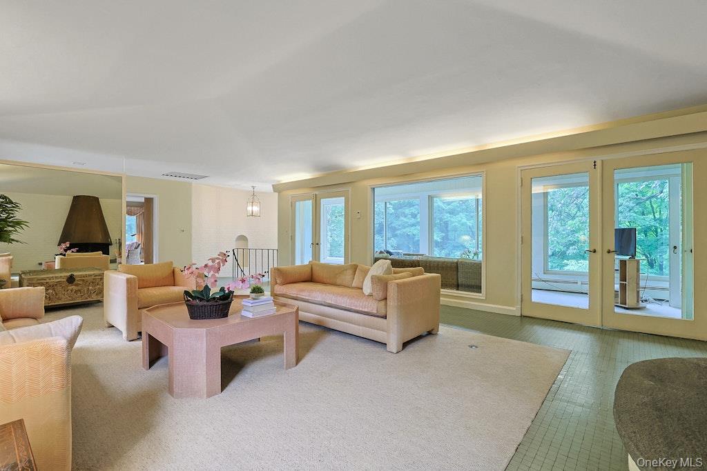 Living room with pale sofas, a pink coffee table, and wide windows overlooking greenery.
