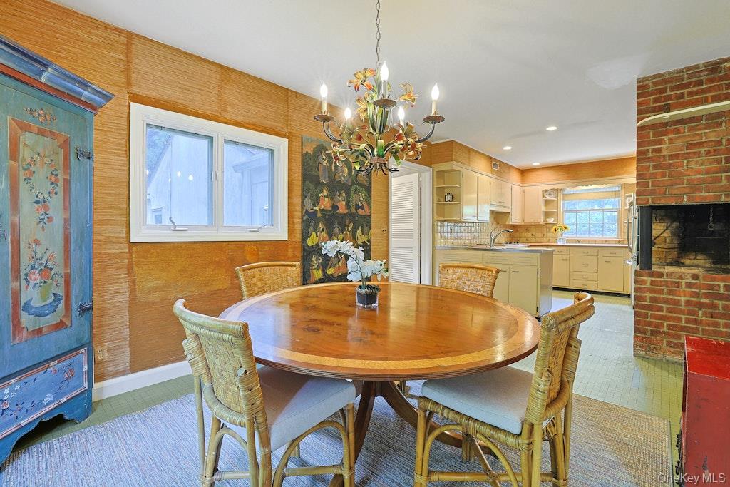 Dining room with a round wooden table, wicker chairs, colorful chandelier, and brick fireplace.