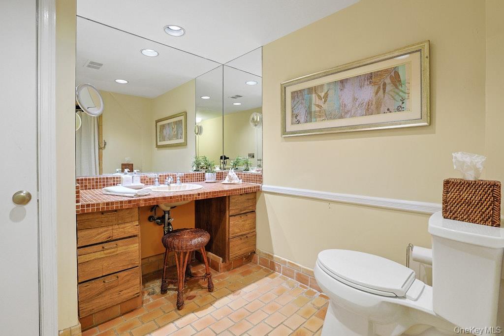 Bathroom with a terracotta-tiled vanity and floor, wood cabinetry, and a large mirror.