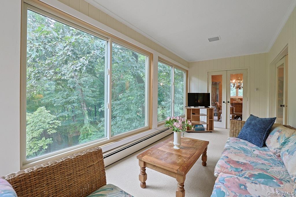Living room with broad windows overlooking leafy trees and wicker and upholstered seating.