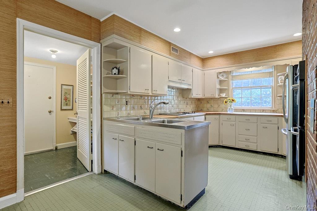 Kitchen with a central double-sink island, white cabinets, patterned backsplash, and green tile floor.