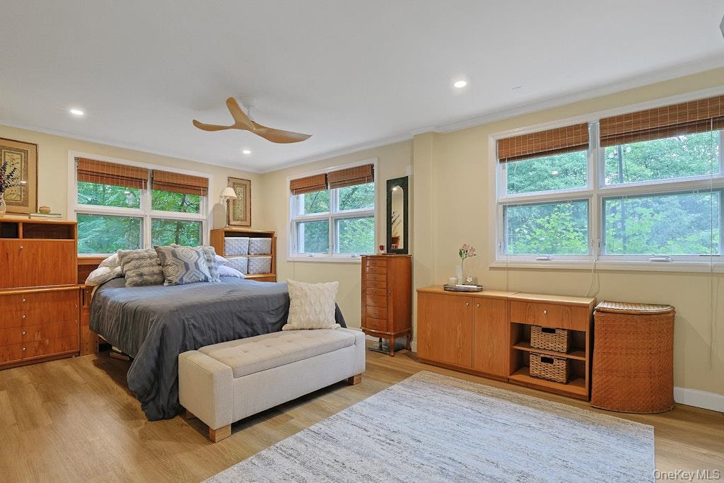 Bedroom with a gray-covered bed, wood furniture, and large windows overlooking leafy trees.