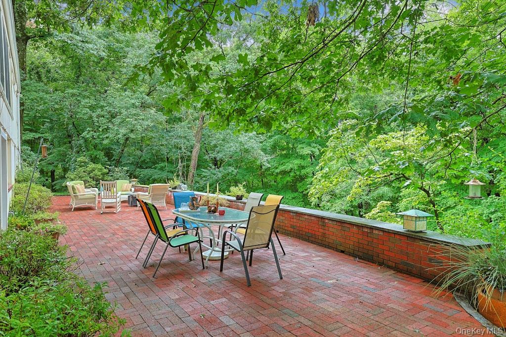 Brick patio with outdoor dining table and chairs, surrounded by mature trees.