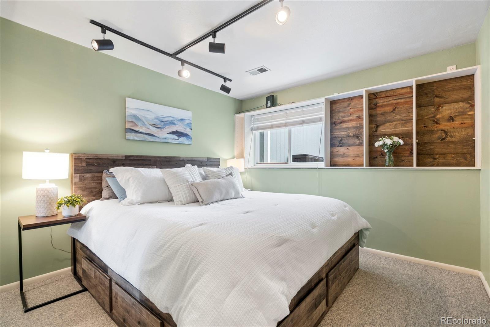 Bedroom with a white-covered wood platform bed, sage-green walls, and built-in wood shelves.